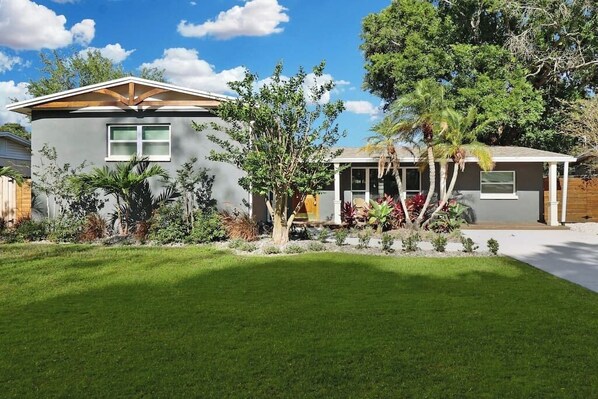 A modern two-story house with a well-maintained lawn and a variety of plants.