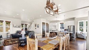 A spacious living room with a wooden dining table, a black leather sofa, and a staircase leading to the upper floor. - Spectacular Views of Long's Peak- 10 min to town-3 full bath plus 2 half bath (Estes Park)