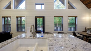 A kitchen with a large granite countertop, a sink, and a dining area with a table and chairs. - It's the Little Things, Creekside, Hot Tub, Firepit, Great Location (Broken Bow)