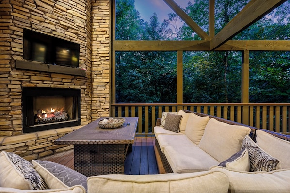 A stone fireplace, a wooden deck, and a cushioned seating area with a view of trees. - It's the Little Things, Creekside, Hot Tub, Firepit, Great Location (Broken Bow)