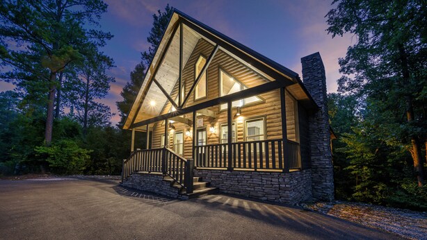 A log cabin with a stone chimney, a wooden deck, and a staircase leading to the entrance. - It's the Little Things, Creekside, Hot Tub, Firepit, Great Location (Broken Bow)
