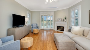 A living room with a flat-screen TV, a fireplace, a ceiling fan, and a view through the glass doors. - Fantastic Marsh View E. Beach-Between Gould's Inlet & Coast Guard. Walk to beach (St. Simons Island)