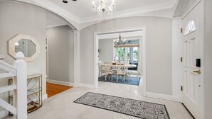 A spacious hallway with a white door, a chandelier, and a dining area visible through an open door. - Fantastic Marsh View E. Beach-Between Gould's Inlet & Coast Guard. Walk to beach (St. Simons Island)
