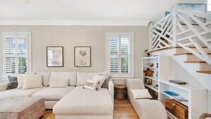 A living room with a sectional sofa, a white staircase, and a bookshelf. - Fantastic Marsh View E. Beach-Between Gould's Inlet & Coast Guard. Walk to beach (St. Simons Island)