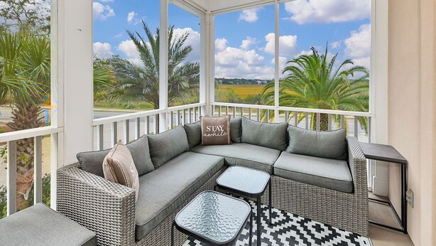 A sunroom with a large window overlooking a landscape, featuring a sectional sofa, two side tables, and a patterned rug. - Fantastic Marsh View E. Beach-Between Gould's Inlet & Coast Guard. Walk to beach (St. Simons Island)