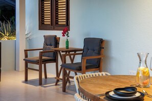 A dining area with wooden chairs and a round table, a vase with flowers, and a bottle of water.