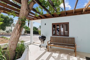 Une terrasse couverte avec un banc en bois, un barbecue et un arbre.