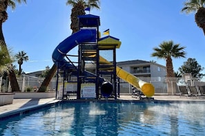 A pool with a water slide and a lifeguard tower.