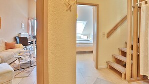 Una sala moderna con un sofá, una mesa de centro y un comedor. Una escalera conduce a un dormitorio con tragaluz.