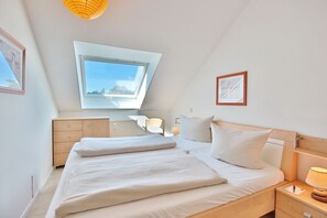Un dormitorio con tragaluces, una cama con almohadas, una mesita de noche con lámpara y un aparador.