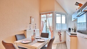 Cocina compacta con comedor, que incluye una mesa para dos, un radiador y una ventana con cortinas.