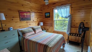 A wooden cabin bedroom with a bed, a nightstand, a dresser, a ceiling fan, and a window with curtains.
