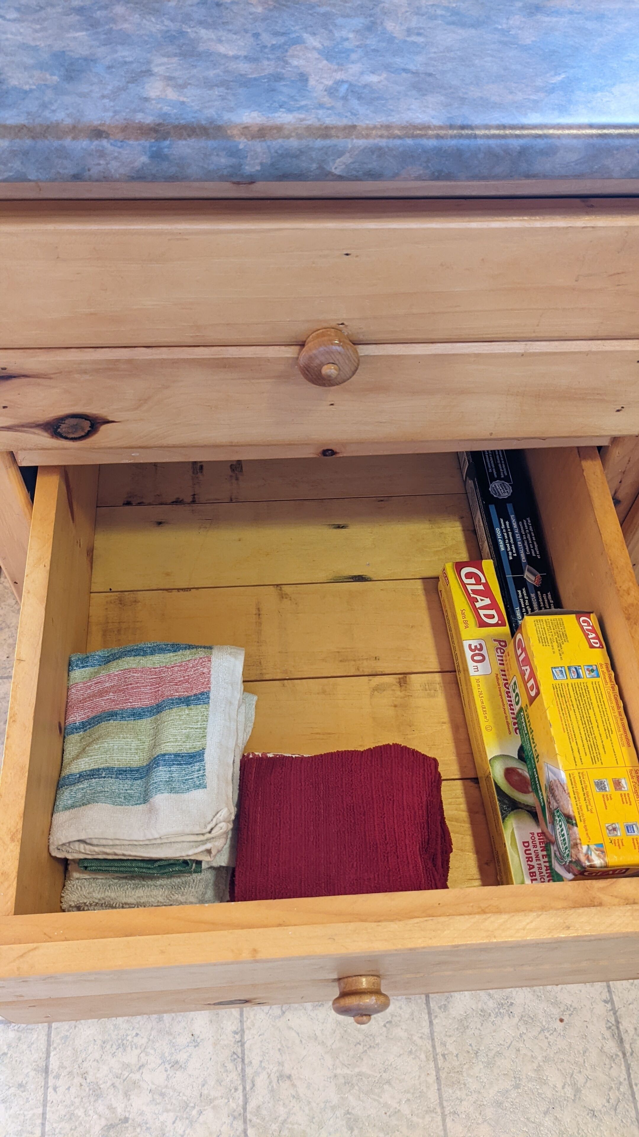 A wooden drawer with a handle, containing folded towels and boxes of GLAD detergent.