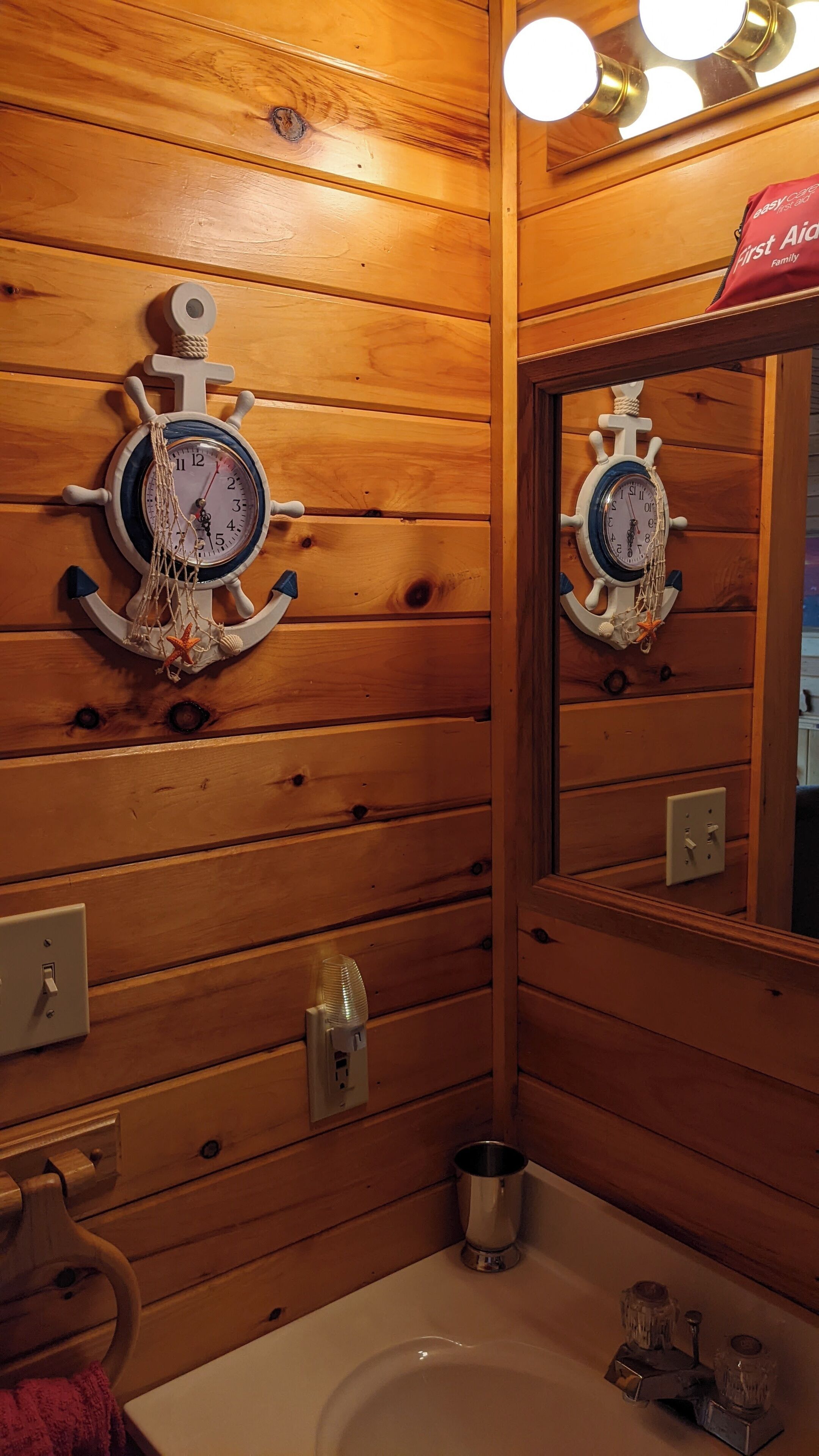 A wooden cabin-style bathroom with a wooden wall, a sink, a mirror, and a clock.