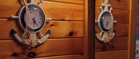 A wooden cabin-style bathroom with a wooden wall, a sink, a mirror, and a clock.