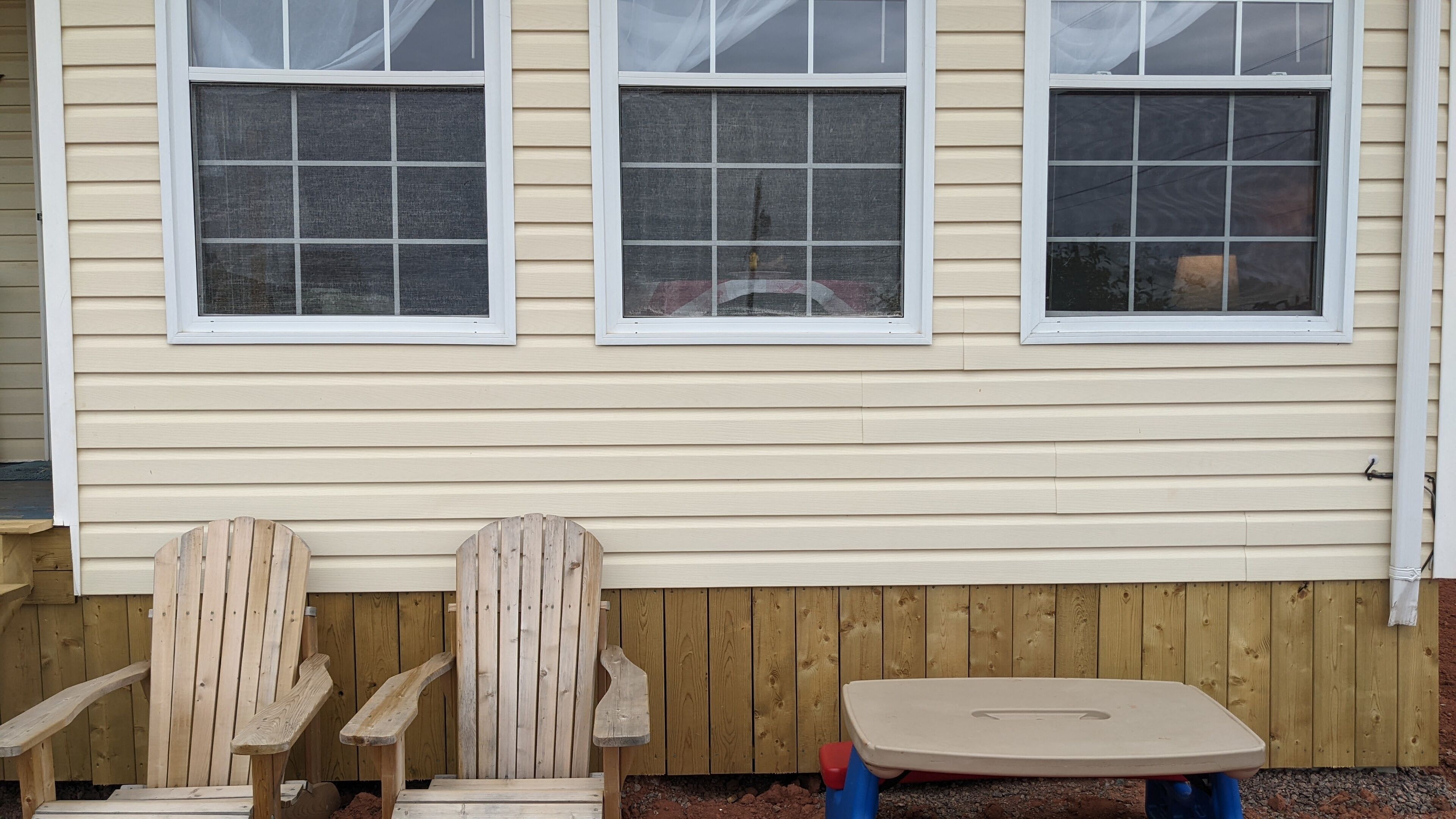 A wooden deck with two Adirondack chairs and a small table.