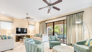 A spacious living room with a ceiling fan, a flat-screen TV, and a large sliding glass door leading to an outdoor area. - Games Room | Private Pool with Built in BBQ | 8 Miles to Disney (Kissimmee)