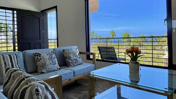 Ein modernes Wohnzimmer mit einer Couch, einem Glastisch und Meerblick durch große Fenster.