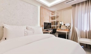 A hotel room with a large bed, a desk with a computer, a chair, and a vanity with a mirror and toiletries.