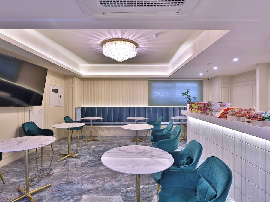 A modern hotel lobby with marble flooring, teal chairs, and a central seating area.