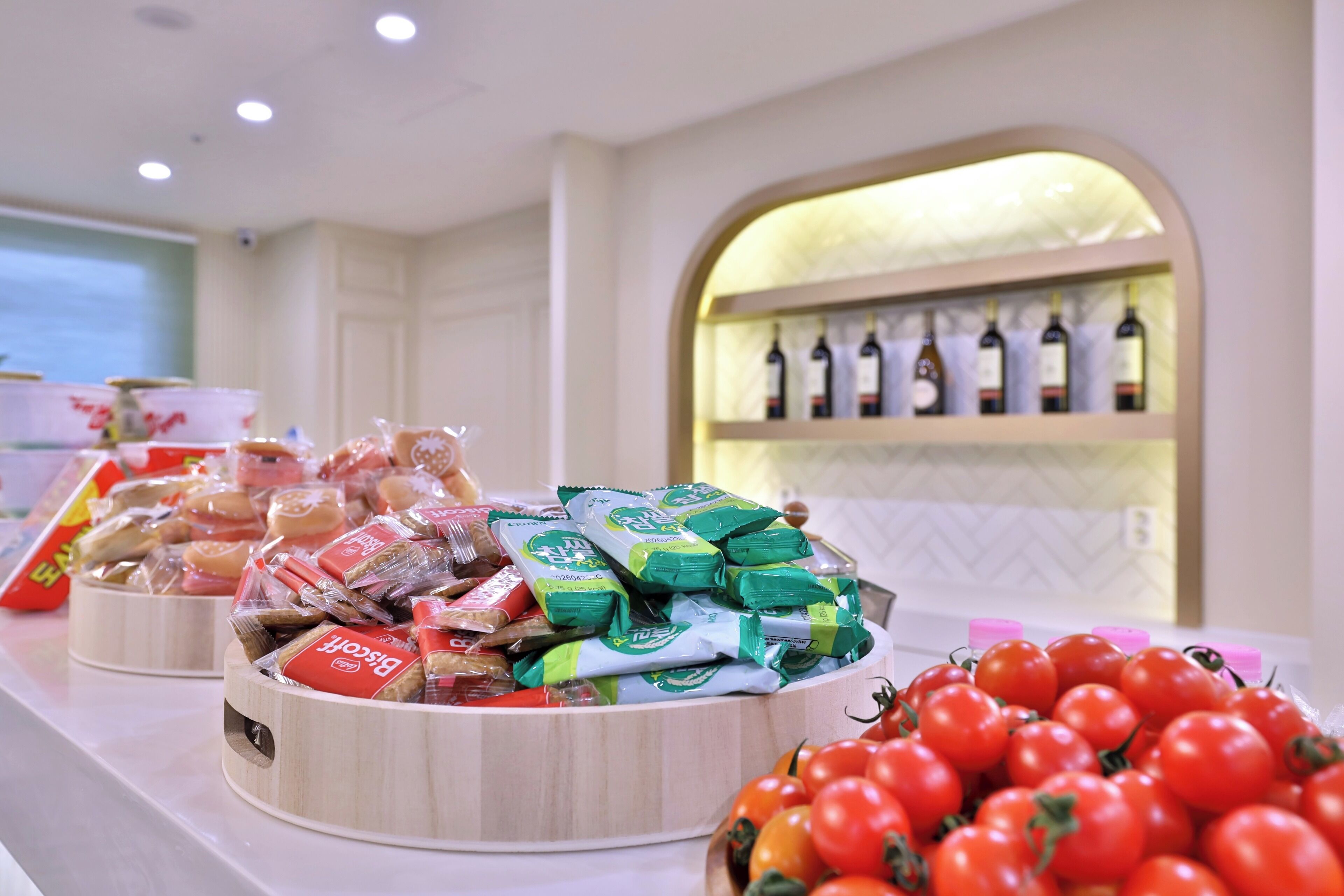 Un bufé con diversos alimentos, incluyendo aperitivos empaquetados, un tazón de tomates y una selección de bebidas en botella.