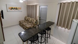 Un espacio habitable compacto con un sofá, una mesa de comedor con taburetes, un ventilador de techo y una puerta con cortina.