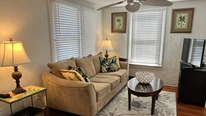 Un salon avec un canapé beige, deux lampes, un téléviseur et un ventilateur de plafond.
