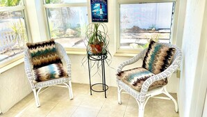 Deux fauteuils en osier avec des coussins à motifs, une petite table sur laquelle est posée une plante en pot, et un panneau orné d’une image de phare.