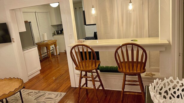 Une cuisine moderne avec des meubles blancs, une table à manger en bois, deux chaises en bois et un petit îlot central doté d’un plan de travail.