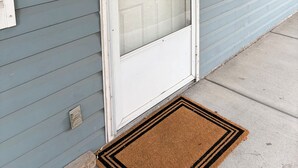 Une maison avec une porte d’entrée blanche, une porte vitrée et une fenêtre avec des volets.