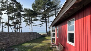 A red building with a bench and a table outside, overlooking a grassy area and trees.