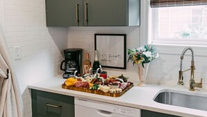 A kitchen with dark green cabinets, a white countertop, a coffee maker, and a wine bottle.