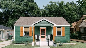 A two-story house with green siding and a gabled roof, featuring a front porch with a small set of steps and a door.