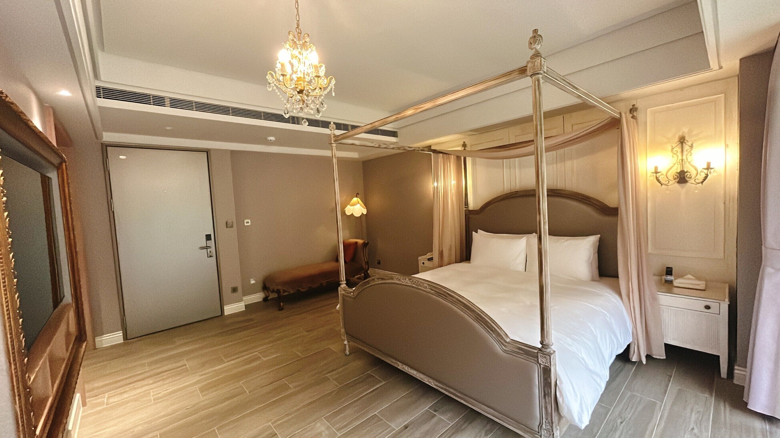 Un lit à baldaquin, un lustre, une table de chevet avec une lampe et un miroir.