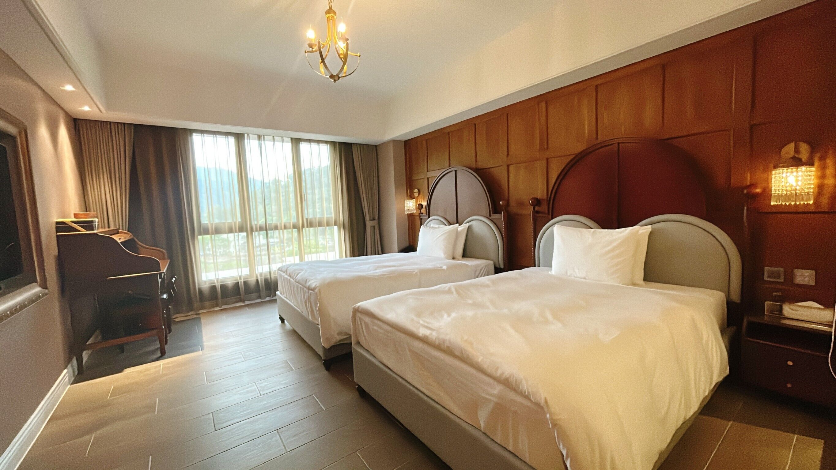 A hotel room with two beds, a piano, and a large window with curtains.