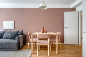 Uma sala moderna com um sofá cinzento, uma mesa de jantar de madeira com cadeiras, uma porta branca e um quadro emoldurado na parede.