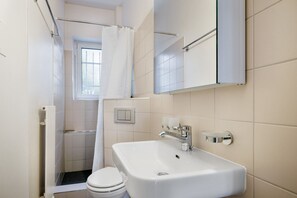 Et lille, moderne badeværelse med hvid vask, toilet og brusebad.