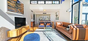 A modern living room with a TV, sofa, ottoman, and dining area.