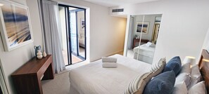 A hotel room with a bed, a wooden nightstand, a mirror, and a view through a sliding door to the outside. - Penthouse Apartment With Massive Private Terrace + Parking + 2 Pools + Views (Rushcutters Bay)