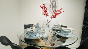 A dining area with a glass table surrounded by black chairs, a framed picture on the wall, and a vase with red flowers. - Cozy, Modern and Centrally Located (Edmonton)
