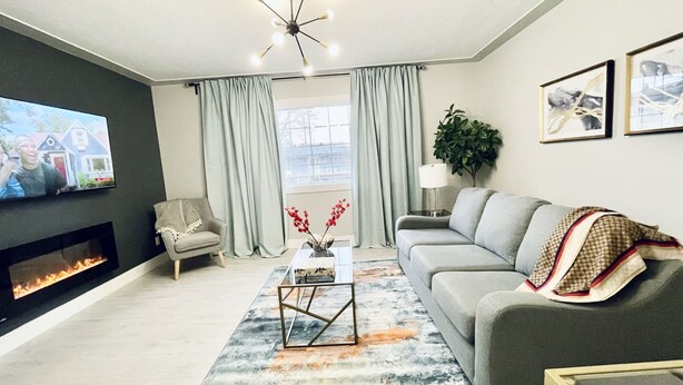 A modern living room with a fireplace, a sofa, a coffee table, and a television. - Cozy, Modern and Centrally Located (Edmonton)