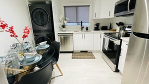 A modern kitchen with white cabinets, stainless steel appliances, and a dining area with a glass table and chairs. - Cozy, Modern and Centrally Located (Edmonton)