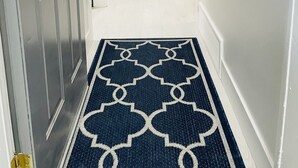 A hallway with a patterned rug, a mirror, and a console table with a vase of red flowers. - Cozy, Modern and Centrally Located (Edmonton)