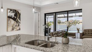 A modern kitchen with granite countertops, stainless steel sinks, and pendant lighting. - Luxury Lakefront Oasis w/ Heated Pool & Spa (Cape Coral)