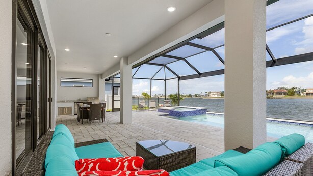 A covered outdoor area with a pool, seating, and a dining area. - Luxury Lakefront Oasis w/ Heated Pool & Spa (Cape Coral)