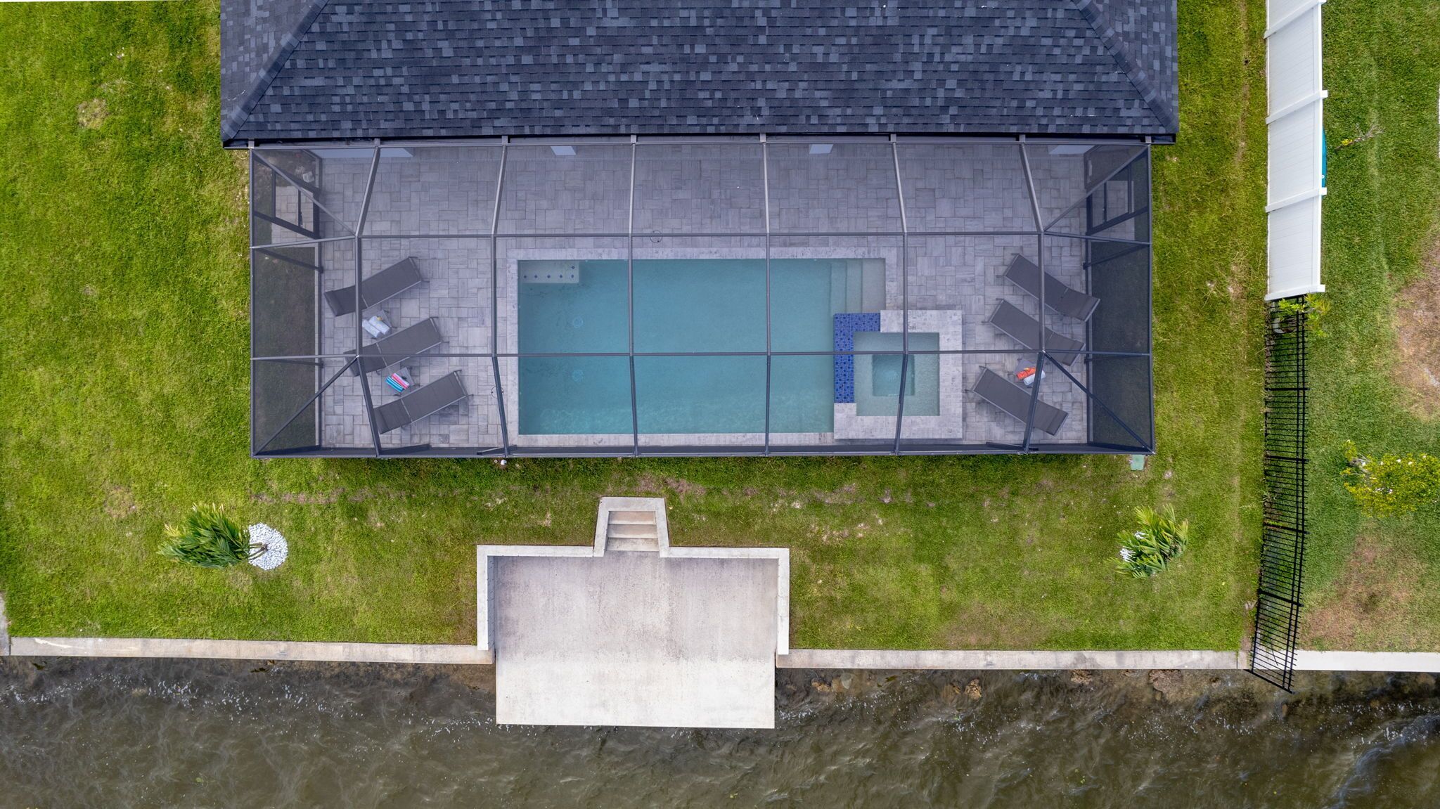 Vue aérienne d’un espace piscine comprenant une terrasse couverte, des sièges et un petit escalier menant à l’entrée de la piscine.
