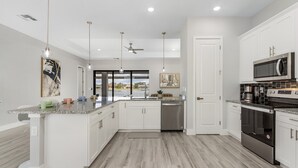 A modern kitchen with white cabinets, stainless steel appliances, and a large island. - Luxury Lakefront Oasis w/ Heated Pool & Spa (Cape Coral)