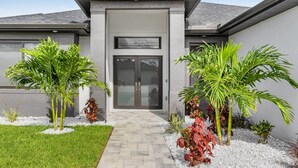 A modern building with a grey facade, a central entrance with glass doors, and a paved pathway leading to the entrance. - Luxury Lakefront Oasis w/ Heated Pool & Spa (Cape Coral)