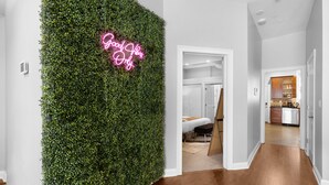 A hallway with a green wall covered in foliage and a neon sign that reads "Good Vibes Only." - 4BD Condo w/Parking & Game Room (Chicago)
