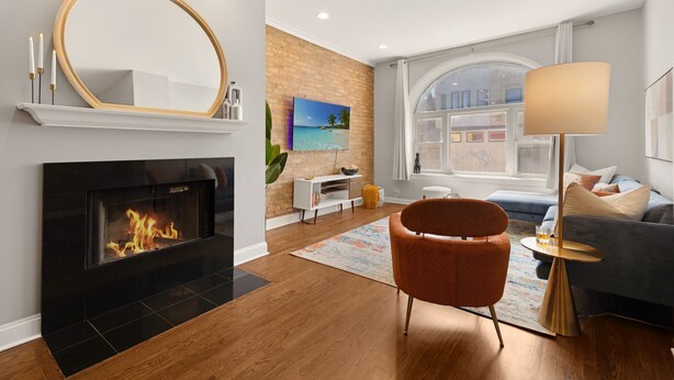 A modern living room with a fireplace, a large mirror, a sofa, a coffee table, and a lamp. - 4BD Condo w/Parking & Game Room (Chicago)
